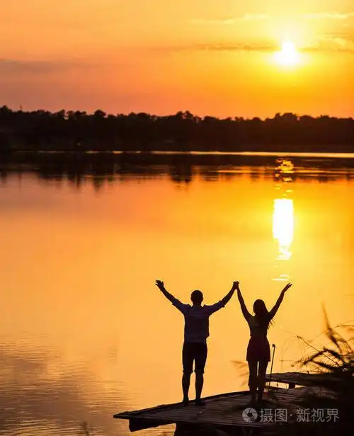 剪影的男女情侣牵手在海滩上,当太阳升起时,爱情和在一起的概念.