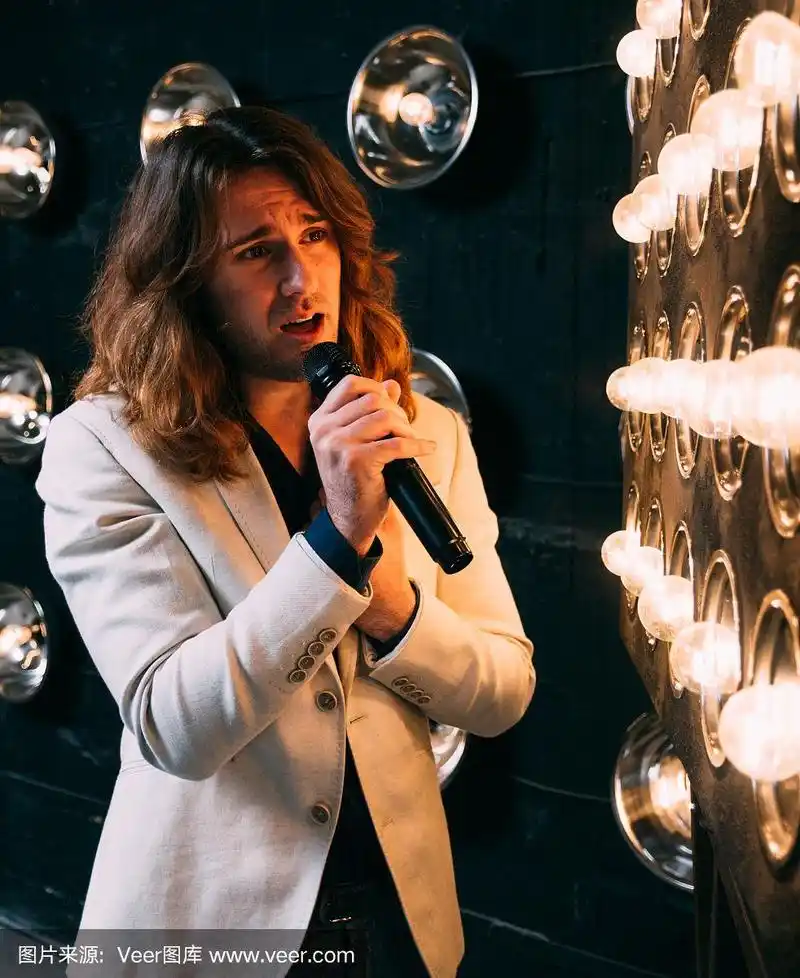 男歌手留着长发,拿着麦克风站在舞台上
