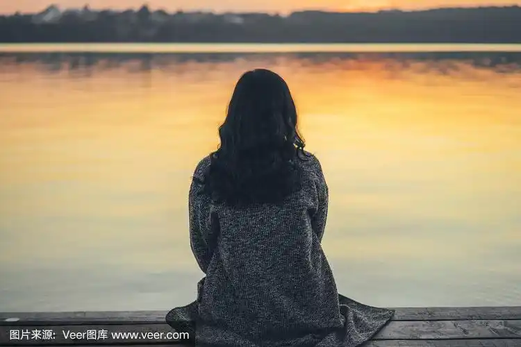 一个长头发的黑发女孩在湖边的码头上休息