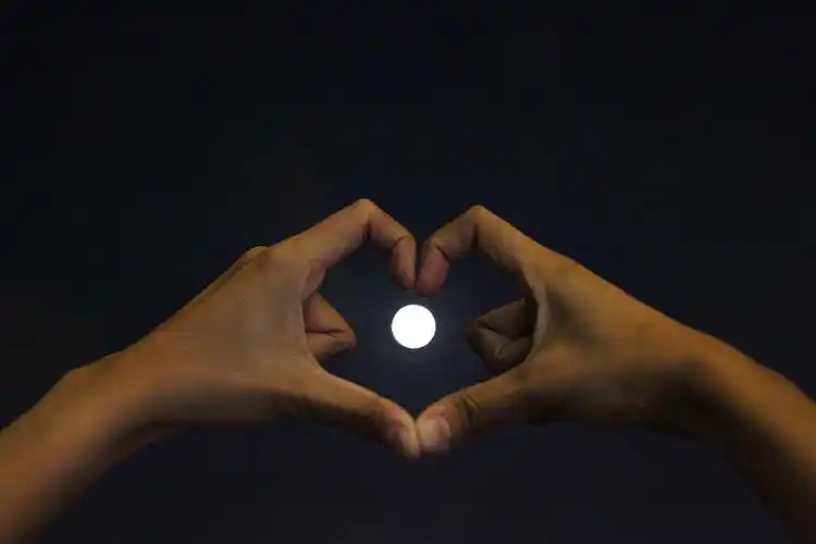 在夜晚的满月下,裁剪的手制作心形图片