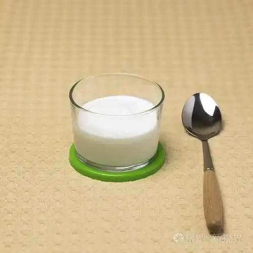 天然奶油酸奶在一个玻璃杯与勺子在厨房的桌子上煮熟的发酵自制