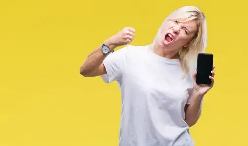 年轻漂亮的金发女郎在孤立的背景上展示智能手机屏幕,愤怒和沮丧,疯狂