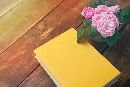 粉红色的玫瑰和书与黄色封面上的木质背景照片