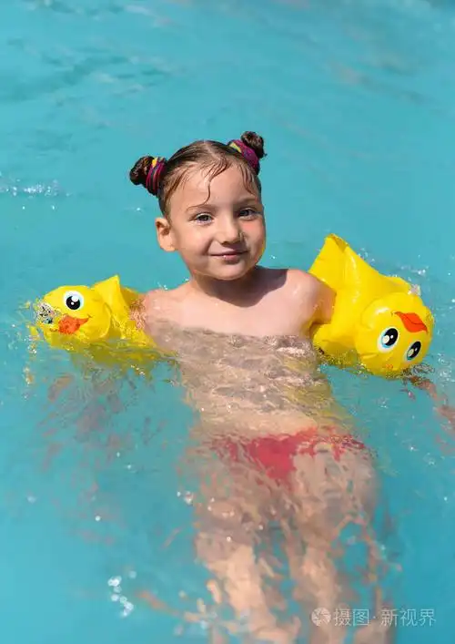 一个阳光明媚的享受玩和在游泳池里打开一个微笑的小女孩照片