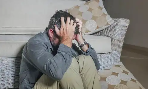 悲伤和沮丧的男人坐在客厅地板上感到绝望和压力,遭受抑郁和焦虑问题