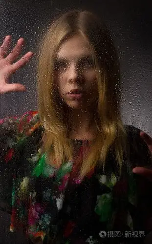 一个漂亮的女孩在黑色背景上淋湿的玻璃后面的肖像