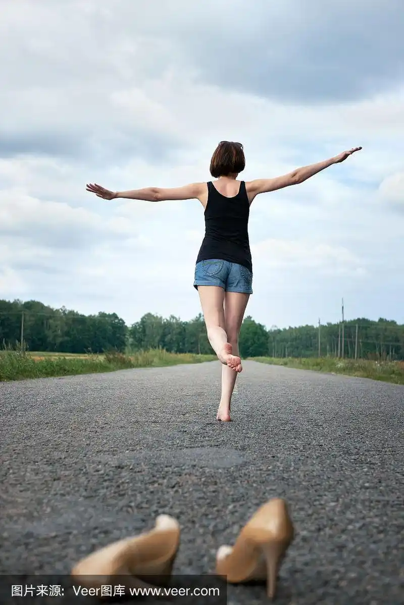 年轻的女孩光着脚走在路上,她把鞋子丢在路上,忘记了夏天和旅行的概念