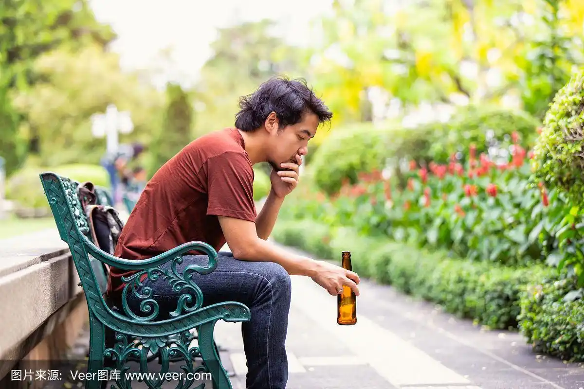 悲伤的单身亚洲男人喝着啤酒坐在公园的地板上.