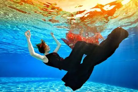 一个年轻的女孩沉入池底,伸出双臂,穿着一件时髦的紫红色连衣裙,一头