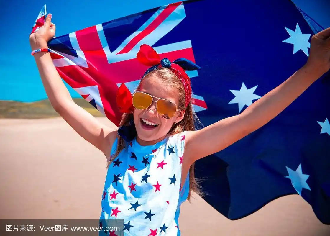 快乐的澳大利亚女孩在蓝天和海洋的背景下,举着飘扬的蓝白红澳大利亚