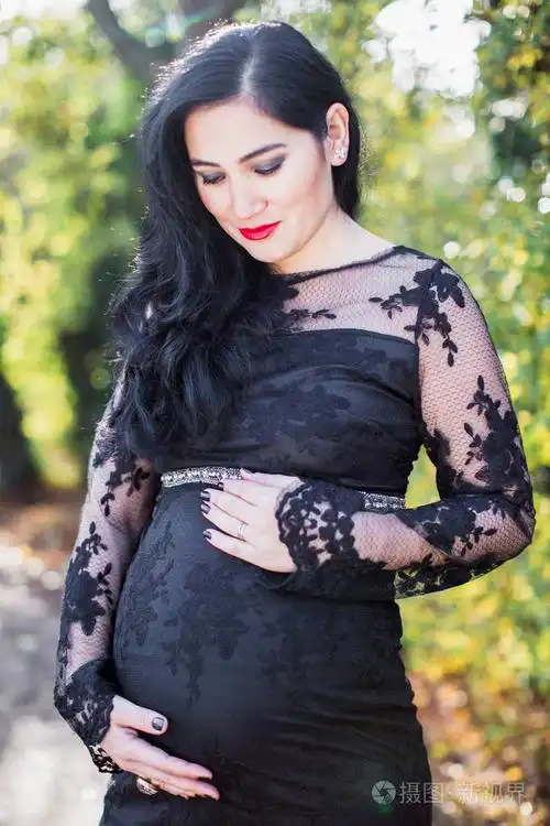 一位怀孕的快乐女人的肖像她站在公园里双手放在腹部