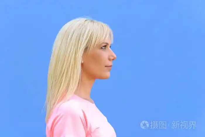 侧面头和肩膀的漂亮年轻的金发女人的肖像, 蓝色背景与复制空间照片