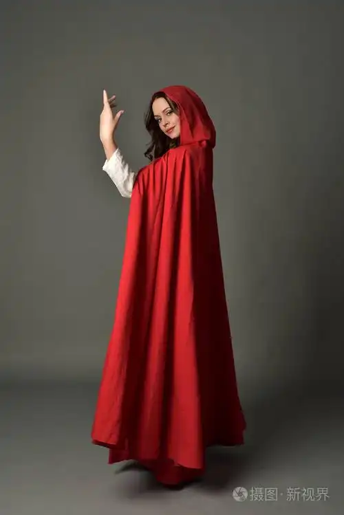穿红色幻想服装的深色女士的全长肖像,披着斗篷,站在灰色工作室背景上