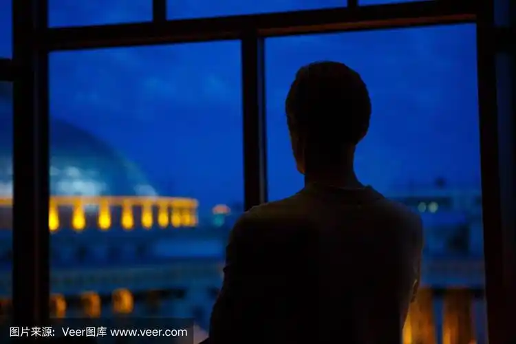 一个人的剪影望着窗外的夜晚城市风景