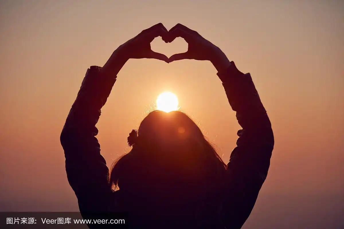 女孩在日落/日出时间用手做心形手势.
