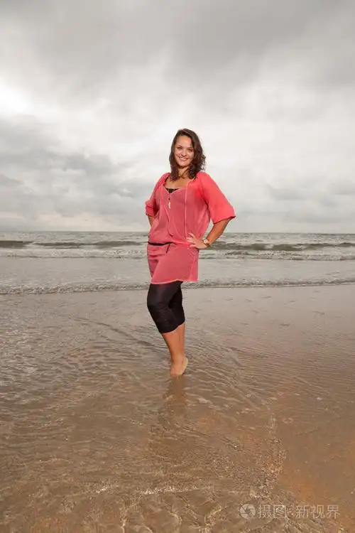 快乐的年轻女人享受海滩附近的户外自然站在水中棕色的头发身穿粉红色