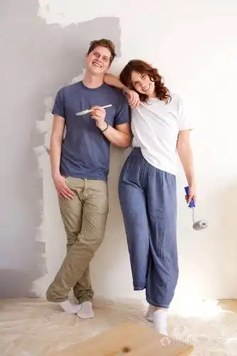 用油漆刷子站在墙边的幸福情侣的全身肖像照片-正版商用图片0ahmt7-摄