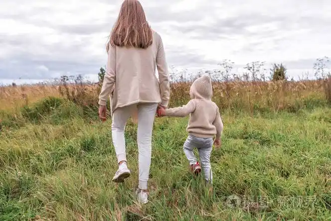 家里的女人妈妈牵着儿子的手小男孩穿着毛衣戴着兜帽在田里休息在田里