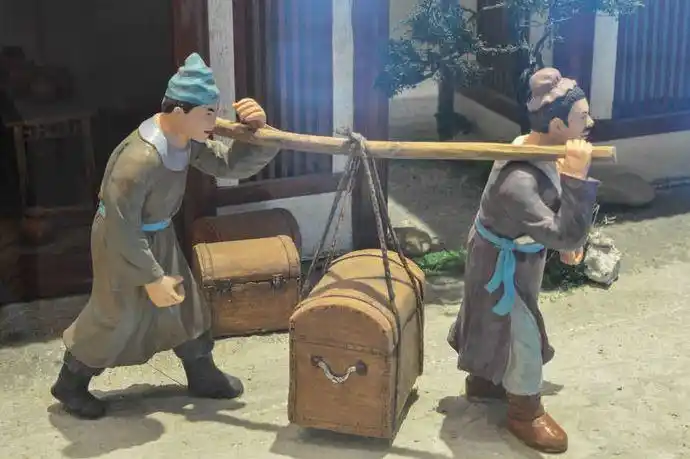 犯人戴着沉重的脚镣,行走费劲.官差拎着两个箱子,苦不堪言.