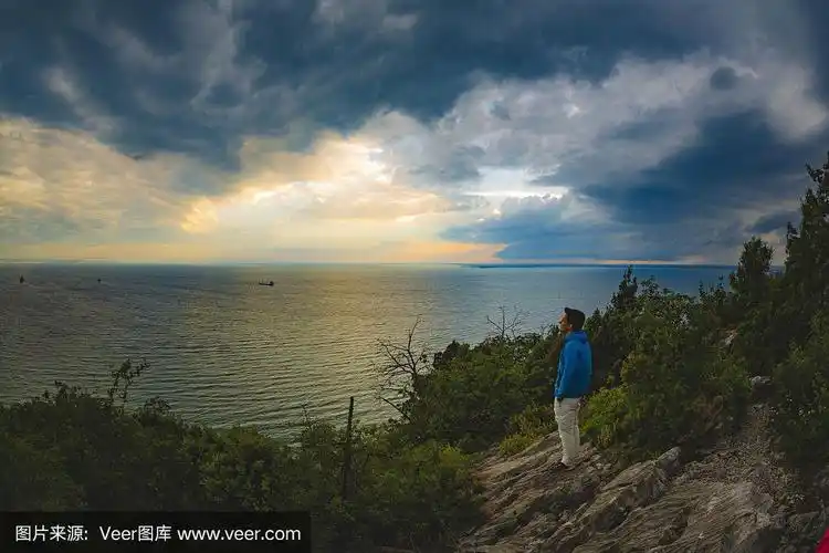 一个年轻人站在高处眺望日落时的大海
