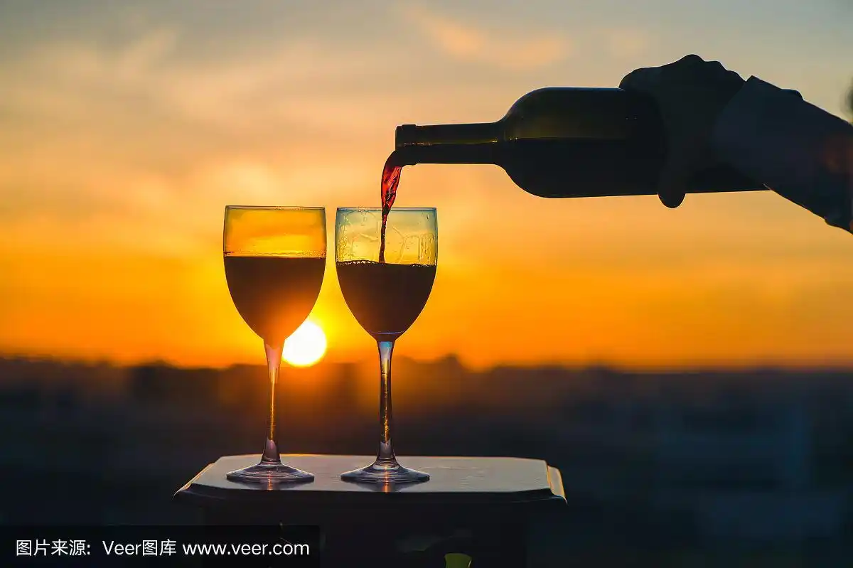 在夕阳的背景下,女性手拿酒瓶将红酒倒入玻璃杯中.