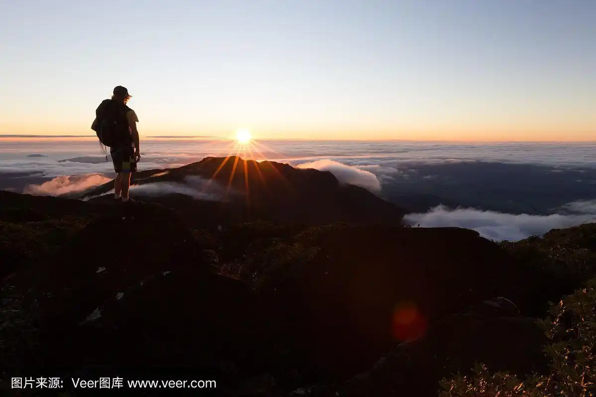 一名登山者在云层上方的制高点上观看太阳升起