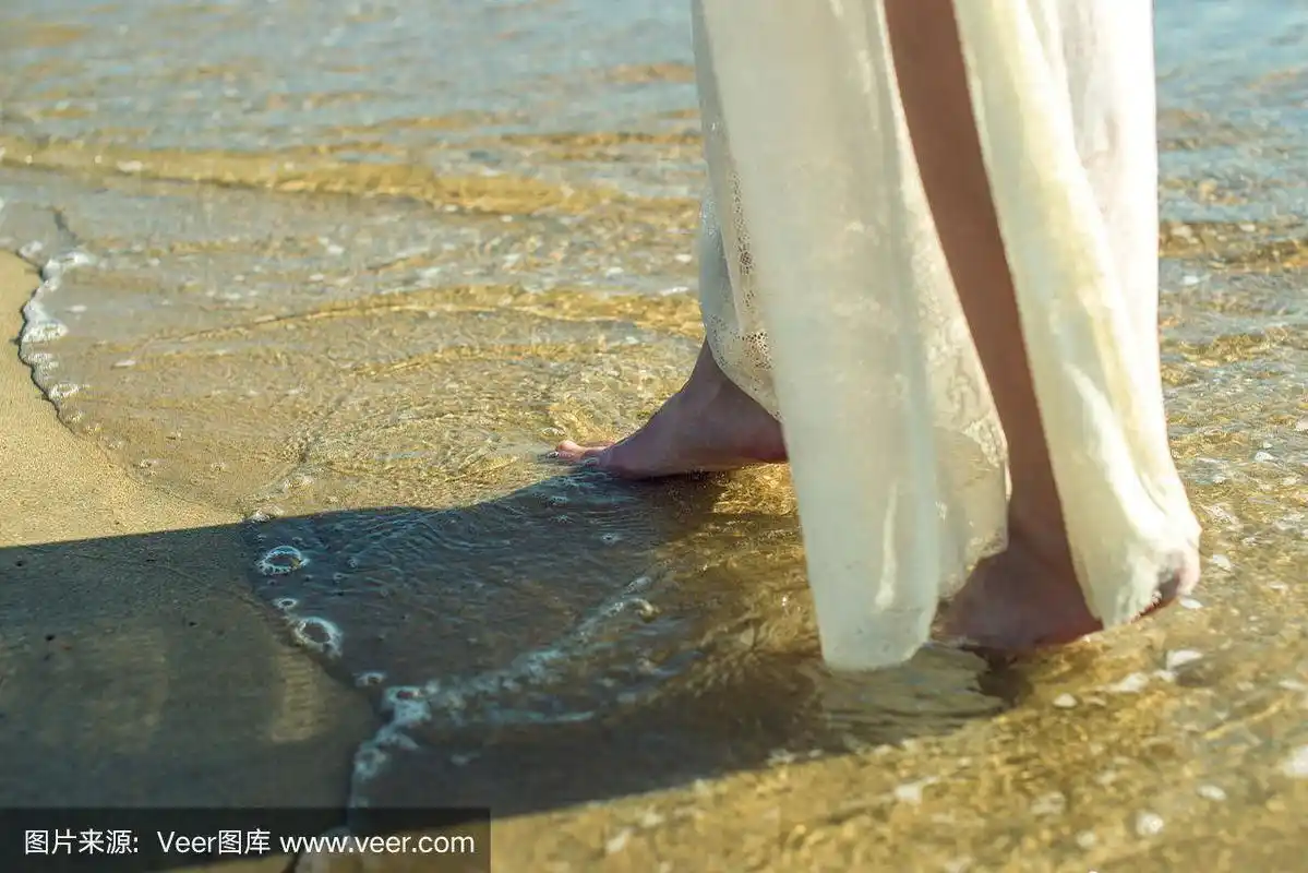 女孩穿着白色的裙子赤脚走在沙滩上