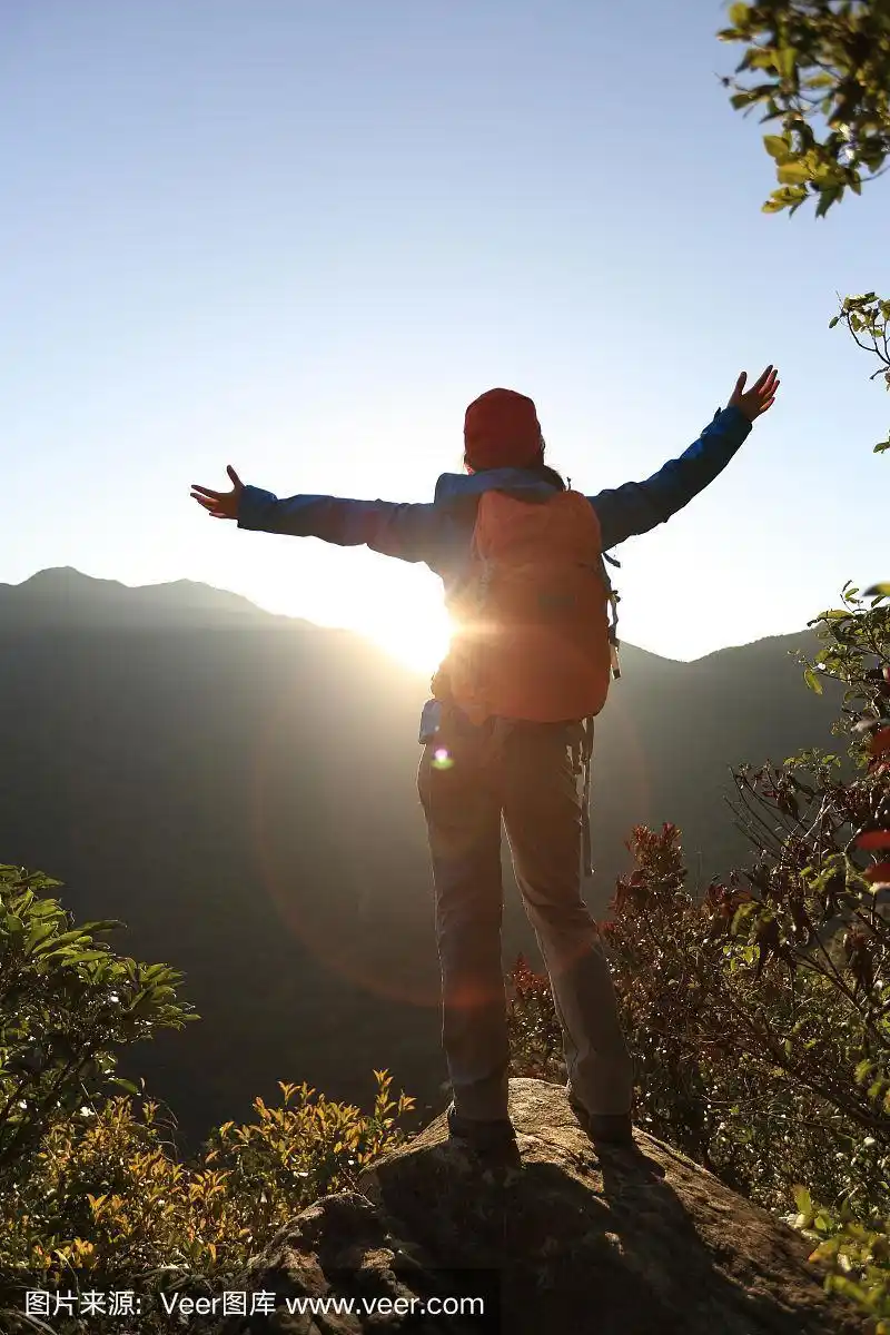成功的女性徒步旅行者在日出的山顶张开双臂