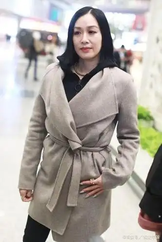 北京,钟丽缇现身机场,她留着齐肩短发身穿米灰色风衣和连帽卫衣,搭配