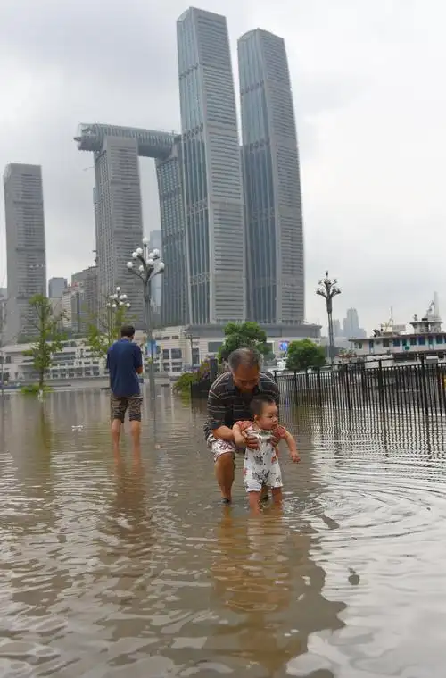 一位老人抱着小孩在洪水淹了的阳光100国际新城广场上戏水