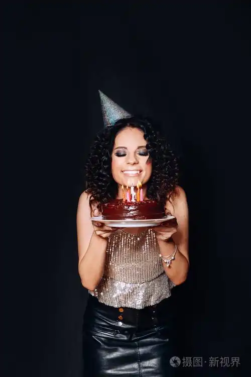一个年轻的美丽的黑发女孩拿着生日蛋糕与蜡烛在黑色背景的肖像