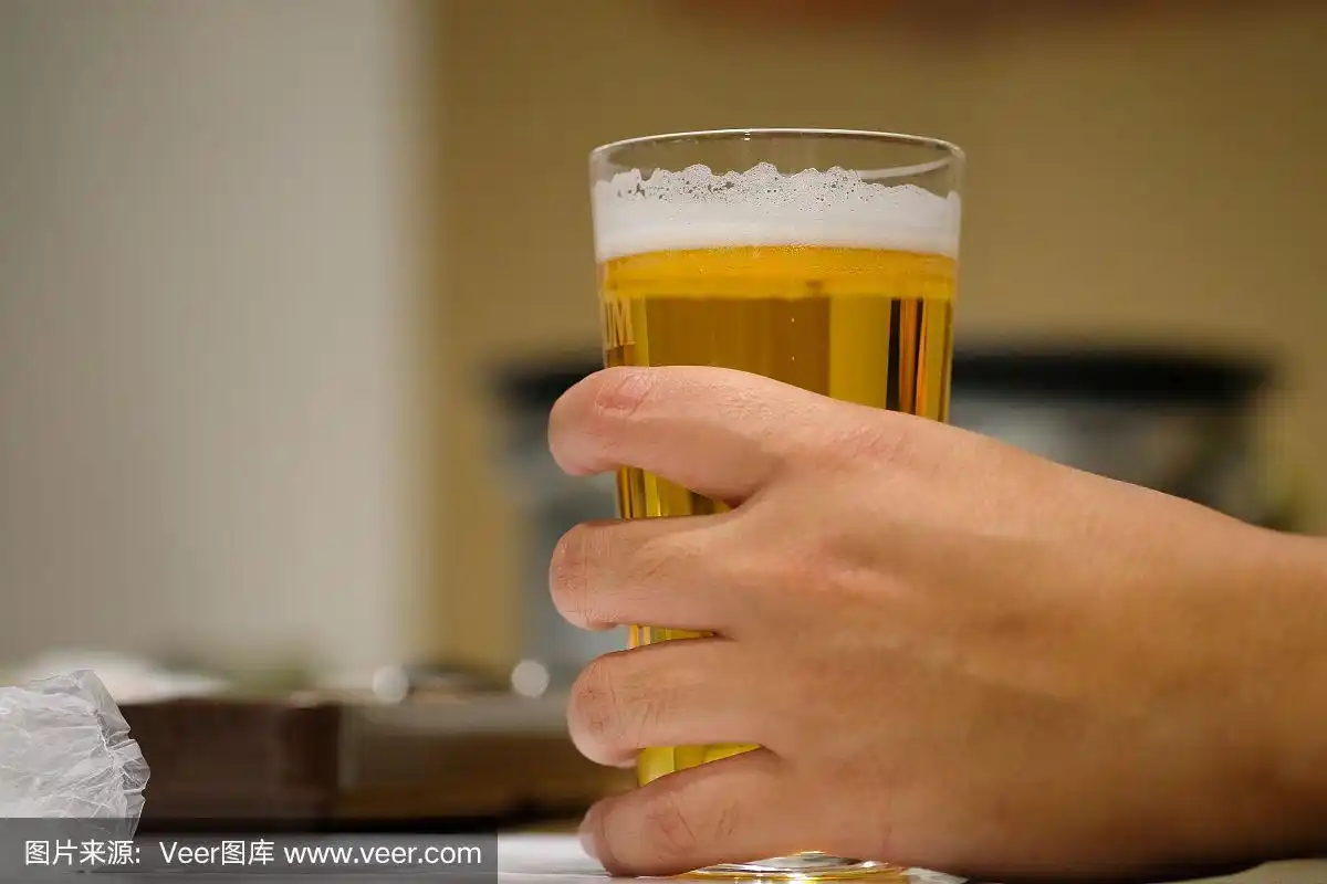 一个男性的手在桌子上拿着一杯啤酒的特写