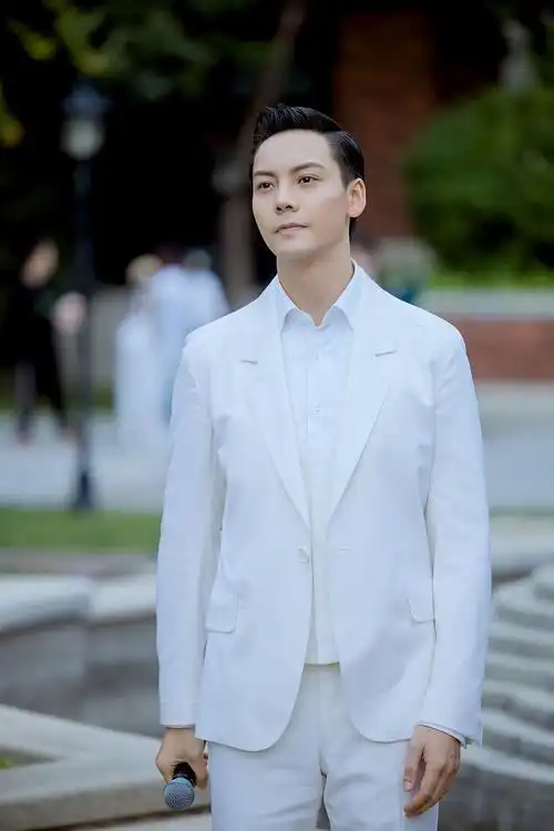 他穿纯白色西装简约清爽,梳油头露坚毅面容,立于墙前倒影氛围感十足.