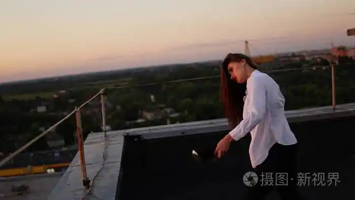 年轻女孩在运动制服坐在屋顶的边缘在日落期间照片-正版商用图片06ij