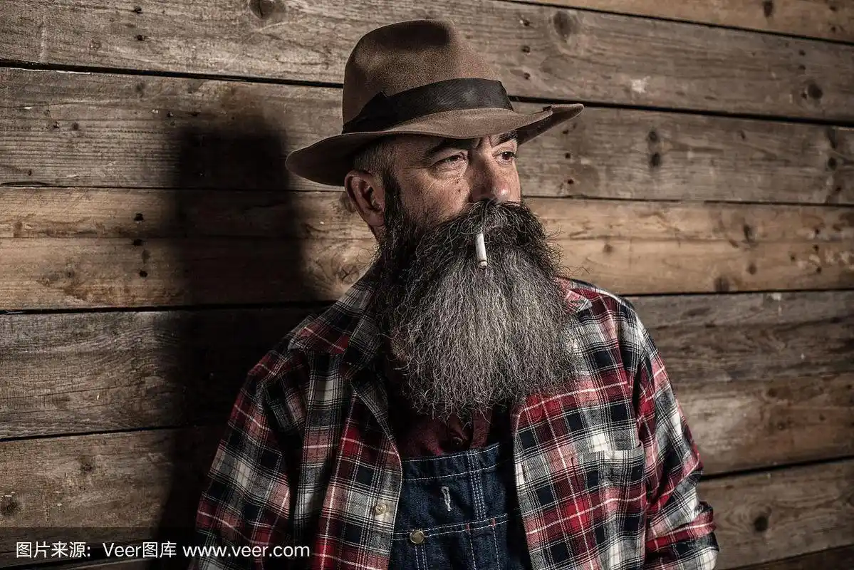 吸烟的老男人,留着长长的灰胡子,穿着牛仔工装裤.