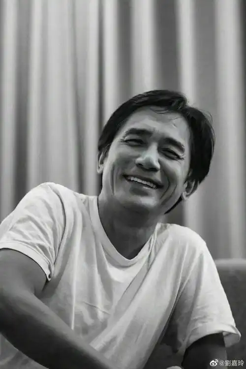 照片中梁朝伟白色短袖,短发素颜,手舞足蹈地与陈可辛导演讨论着什么