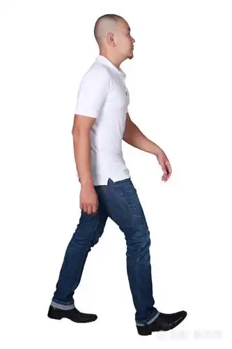 身着白色马球衫和牛仔裤行走的秃头亚裔男子的全身肖像, 侧面视图被