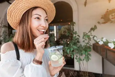 亚洲妇女在城市街道户外喝黄瓜柠檬水排毒饮料的特写镜头照片