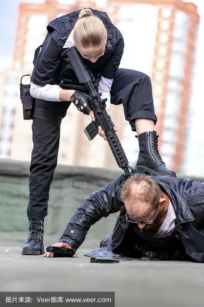 女士兵,间谍杀手或女警察手里拿着枪,用枪指着躺在地上的一个男人