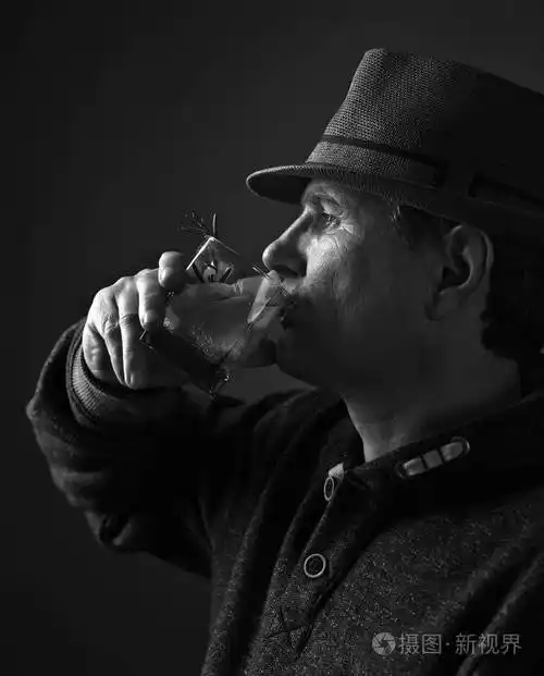 戴着帽子的中年男人喝着一杯带柠檬的酒精鸡尾酒黑白的