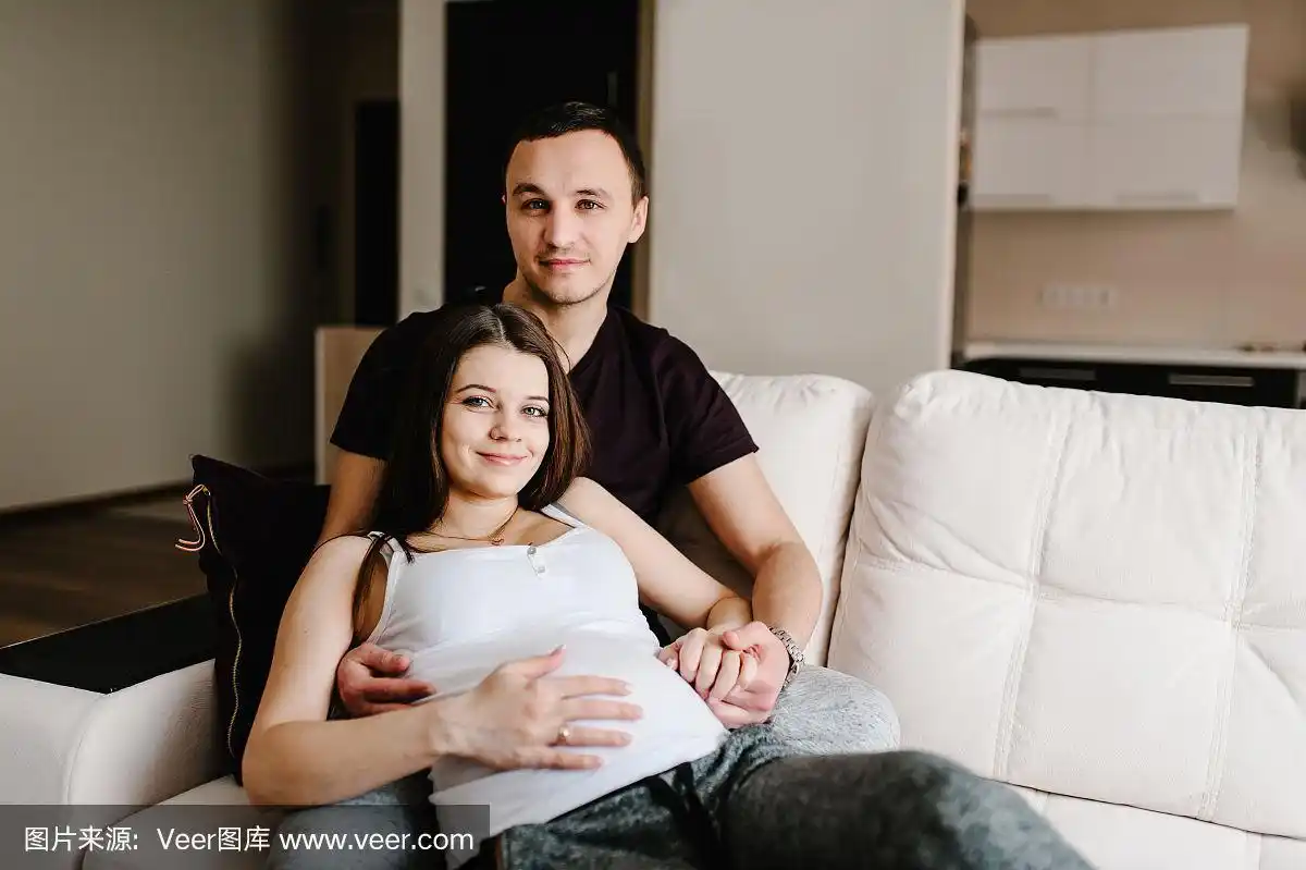 孕妇和可爱的帅哥在家里抱着肚子.爱的夫妻.亲子关系的概念.婴儿洗澡.